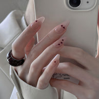 Glossy medium almond nails with nude base and tiny red hearts for a soft, romantic vibe.