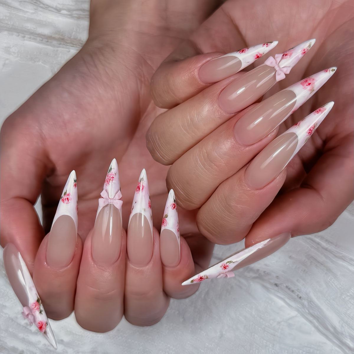 Glossy extra-long stiletto nails with nude base, floral French tips, and 3D pink bows for a romantic, feminine vibe.