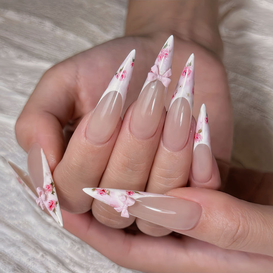 Glossy extra-long stiletto nails with nude base, floral French tips, and 3D pink bows for a romantic, feminine vibe.