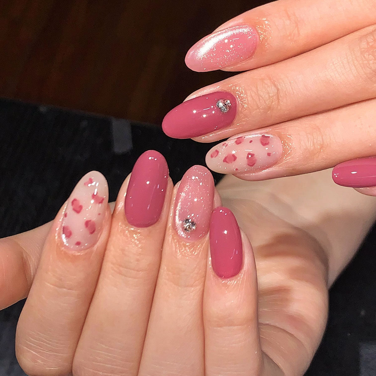 Oval-shaped press-on nails in rose pink, with glitter, petal print, and silver rhinestone details