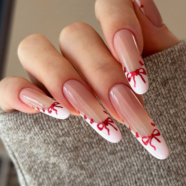 Glossy extra-long stiletto nails with nude base, white French tips, and hand-painted red hearts & bows for a sweet, romantic vibe.
