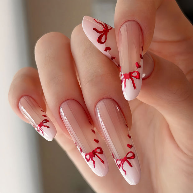 Glossy extra-long stiletto nails with nude base, white French tips, and hand-painted red hearts & bows for a sweet, romantic vibe.
