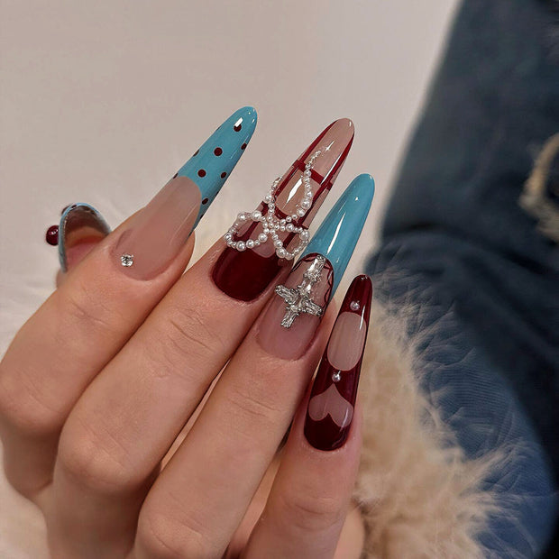 Glossy extra-long stiletto nails with cyan and crimson contrast, decorated with polka dots, hearts, pearls, and crystal crosses for a bold, sweet look.