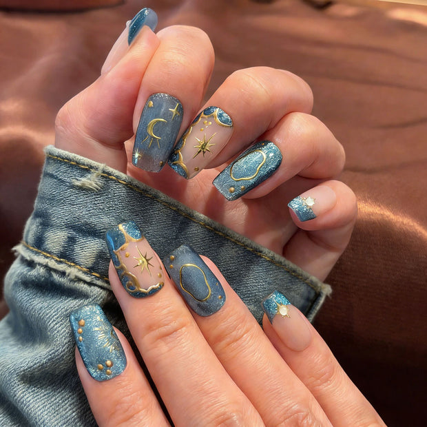 Celestial-inspired press-on nails: nude-blue gradient with gold star/moon motifs, perfect for parties.